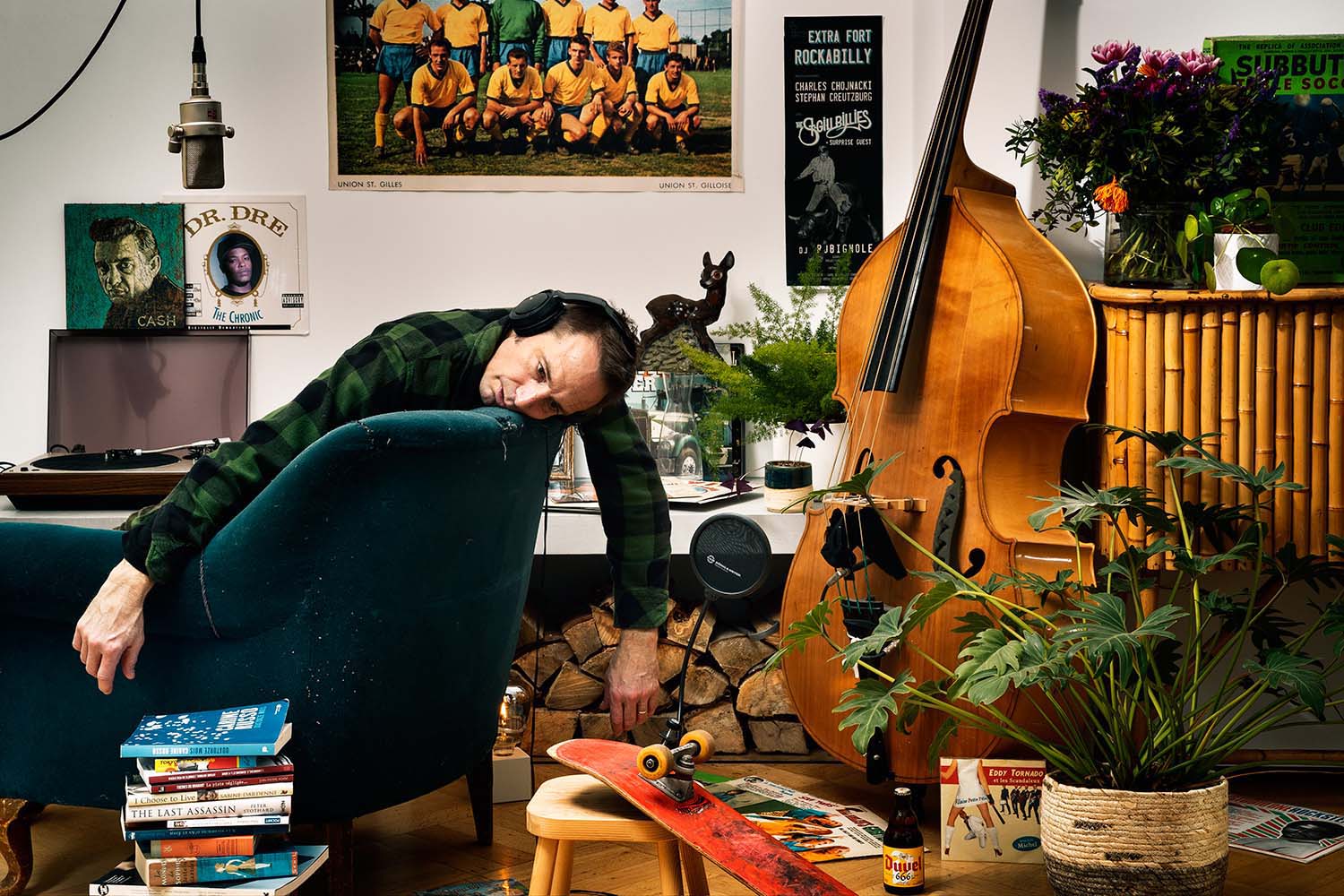 Funny picture of Matt Graves, the founder of Frissons Media. He strangely sits on a sofa. There are plenty of music records, some microphones, a double bass, plants, a skateboard, a poster of l'Union Saint-Gilloise football team, a tiki bar